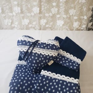 May include: A navy blue fabric set featuring a heart-shaped pillow and two towels, all decorated with a white diamond pattern and white lace trim. The heart pillow includes a dark blue hanging loop and a small rectangular brand tag on the side.