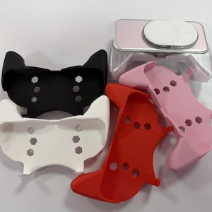 May include: A collection of colourful phone accessories, including black, white, red, and pink protective cases. A pink phone with a white circular button is also visible. The cases have a unique design with hexagonal cutouts.