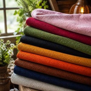 Könnte beinhalten: Ein Stapel farbiger, strukturierter Stoffe in Rosa, Rot, Grün, Schwarz, Orange, Braun, Marineblau und Hellgrau. Die Stoffe sind ordentlich gefaltet und übereinander gestapelt, wodurch eine Vielzahl von Farben und Texturen gezeigt wird.