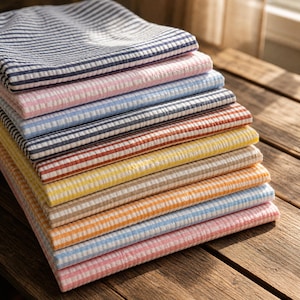 May include: A stack of folded, striped fabric in various colors, including navy, pink, blue, and yellow. The fabric has a textured appearance and is neatly arranged on a wooden surface. The stripes are evenly spaced and create a visually appealing pattern.