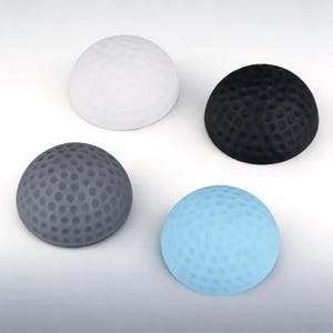 May include: Four golf ball-shaped door stops in white, black, gray, and light blue. Each stop has a dimpled surface, similar to a golf ball. The door stops are made of a soft material and are designed to prevent doors from slamming.