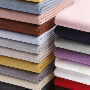 K&ouml;nnte beinhalten: Gestapelte, gefaltete Stoffe in verschiedenen Farben, darunter Gelb, Blau, Rosa, Braun und Rot. Der Stoff scheint ein weiches, filzartiges Material zu sein, wobei jeder Stapel ordentlich angeordnet ist. Das Bild zeigt eine Vielzahl von Farben und Texturen.
