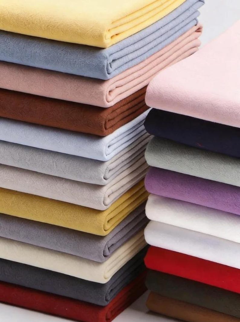 K&ouml;nnte beinhalten: Gestapelte, gefaltete Stoffe in verschiedenen Farben, darunter Gelb, Blau, Rosa, Braun und Rot. Der Stoff scheint ein weiches, filzartiges Material zu sein, wobei jeder Stapel ordentlich angeordnet ist. Das Bild zeigt eine Vielzahl von Farben und Texturen.
