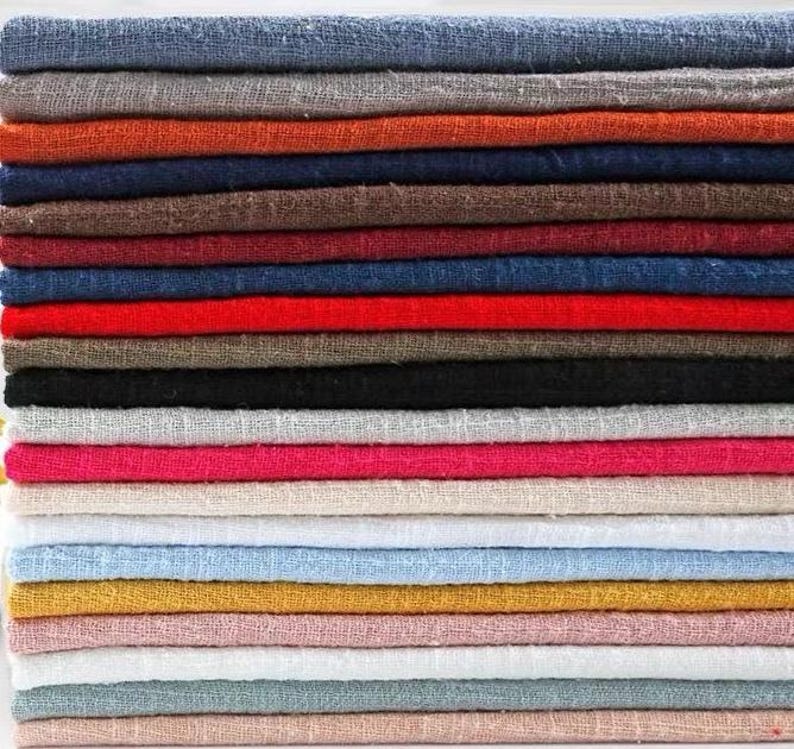 May include: A stack of folded fabric pieces in a variety of solid colors including blue, gray, orange, brown, red, black, white, pink, beige, yellow, and light green. Each piece of fabric features a visible woven texture with a loose, open weave.