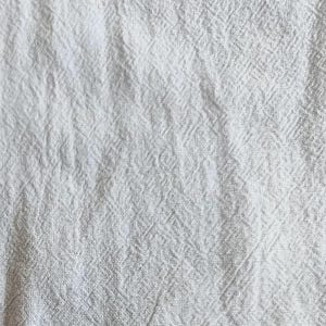 K&ouml;nnte beinhalten: Nahaufnahme eines wei&szlig;en, strukturierten Stoffes mit einem dezenten Webmuster. Der Stoff wirkt weich und leicht zerknittert, was darauf hindeutet, dass es sich um Leinen oder ein &auml;hnliches Material handeln k&ouml;nnte. Der Gesamteindruck ist ein sauberer, neutraler Textil.