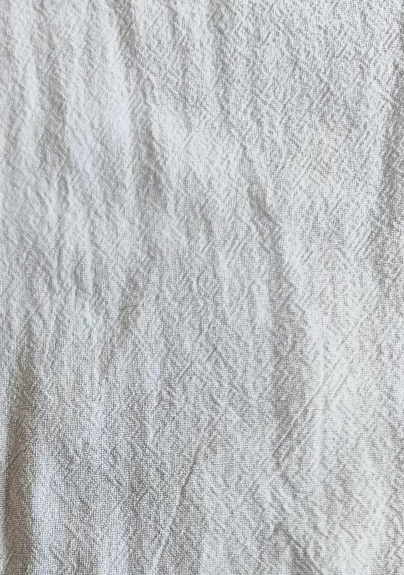 K&ouml;nnte beinhalten: Nahaufnahme eines wei&szlig;en, strukturierten Stoffes mit einem dezenten Webmuster. Der Stoff wirkt weich und leicht zerknittert, was darauf hindeutet, dass es sich um Leinen oder ein &auml;hnliches Material handeln k&ouml;nnte. Der Gesamteindruck ist ein sauberer, neutraler Textil.