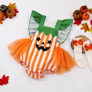 May include: A sleeveless romper featuring a white and orange vertical striped pattern with a jack-o'-lantern face graphic, green ruffled shoulder straps, and an orange glittery tulle skirt overlay, accompanied by two white lace socks with orange bows.