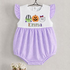 May include: A white and purple striped bubble romper featuring ruffled sleeves and an embroidered Halloween design of a green monster, an orange pumpkin, and a white mummy. The name Emma is embroidered in multicoloured letters below the icons.