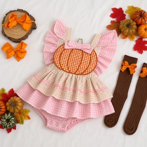 May include: A baby romper featuring a pink and white gingham pattern with ruffled sleeves, a central orange gingham pumpkin applique, and a tiered skirt. The set includes two brown ribbed knee-high socks with orange bows and two orange hair bows.