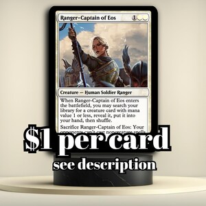 May include: A Magic: The Gathering card titled "Ranger-Captain of Eos." The card features a female character in armor holding a staff. The text on the card describes its abilities. The card is displayed on a black stand.