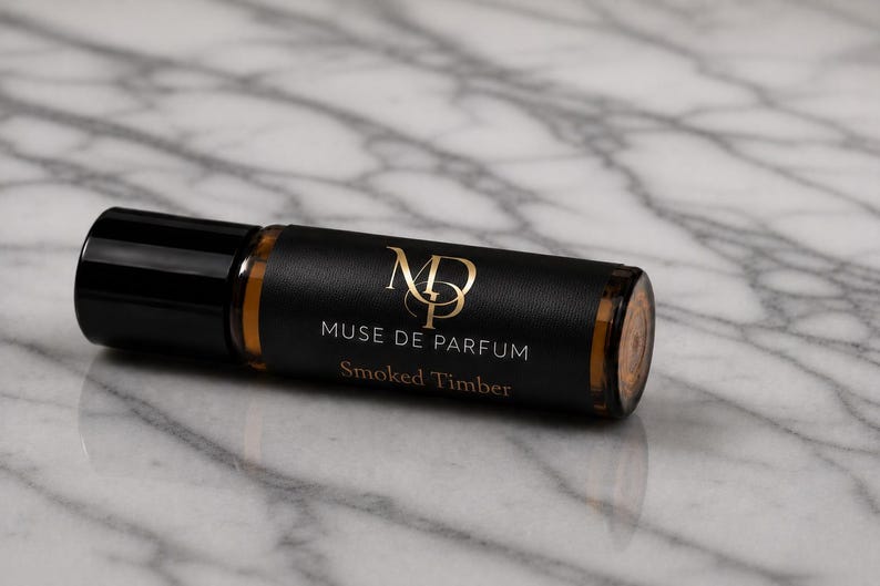May include: A roll-on perfume bottle with a black cap and a black label with gold lettering. The label reads "Muse de Parfum" and "Smoked Timber". The bottle is on a marble surface.