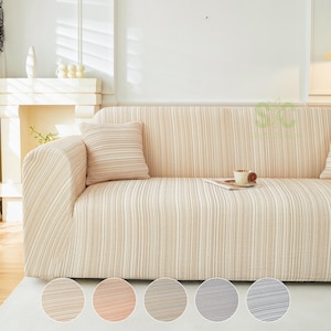 May include: A beige and white striped sofa cover featuring a textured fabric pattern. The cover is fitted over a sofa and includes a matching square throw pillow. Five circular color swatches are displayed at the bottom of the image.