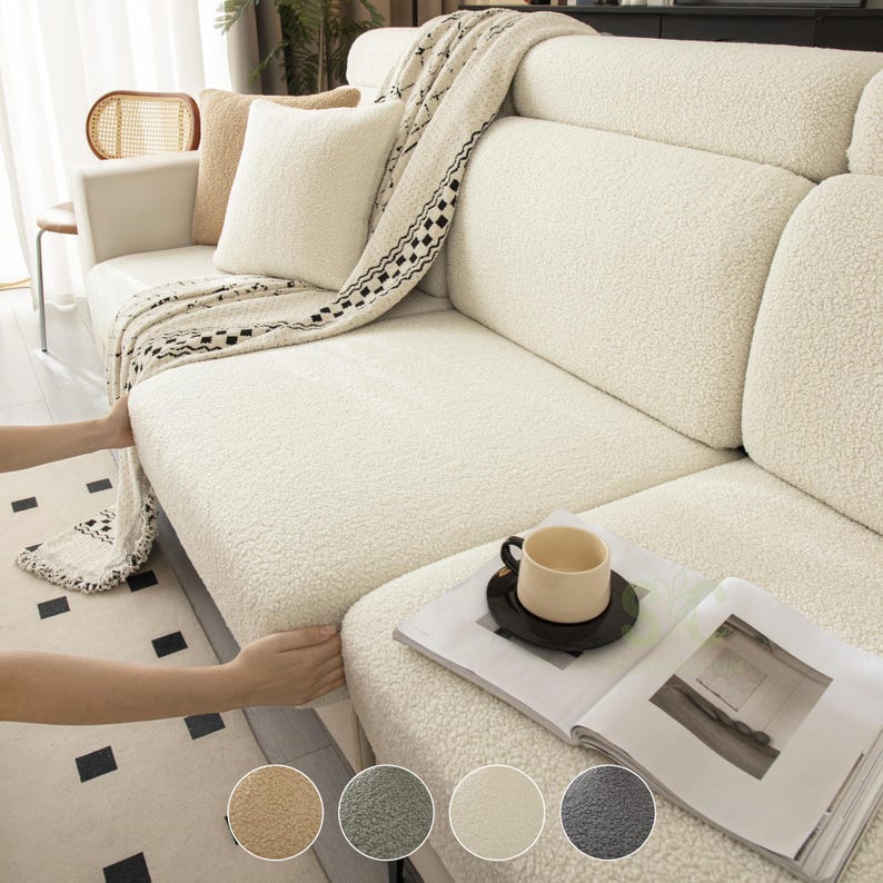 May include: A cream-colored, textured sherpa sofa cover draped over a couch. The cover features a soft, fleece-like material with a nubby surface. A matching throw blanket with a black and white geometric pattern is layered on top of the sofa.