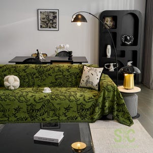 以下が含まれることがあります： 黒い虎模様の緑色のソファブランケットがソファを覆っています。シマウマのデザインの白いクッションがソファにあります。黒いコーヒーテーブルと黒いフロアランプが部屋にあります。