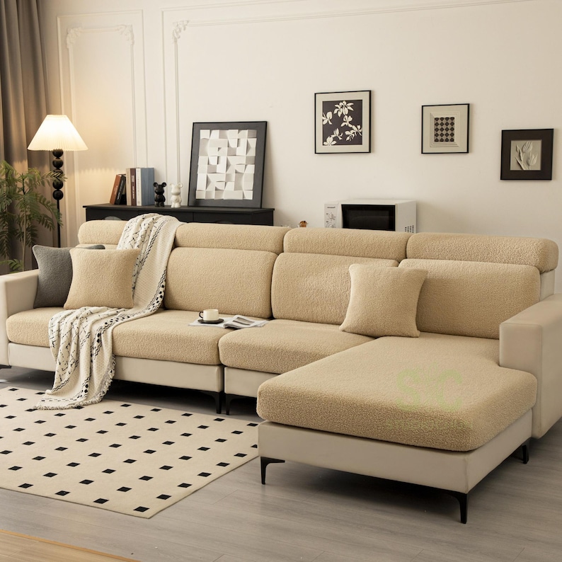 May include: A beige sectional sofa covered in a textured, fleece-like fabric. The sofa features multiple seat cushions, a chaise lounge section, and two matching square throw pillows. A white throw blanket with a black pattern is draped over one side.