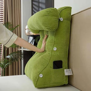 May include: A vibrant lime green corduroy backrest cushion with a headrest and a pocket. The cushion features white buttons and is designed for support while sitting up in bed or on a sofa. The cushion is shown on a beige surface.