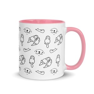 May include: White ceramic mug with a pink interior and handle. The mug features a repeating pattern of black line drawings of otters in various poses. The otters have small, detailed faces and are in different positions.
