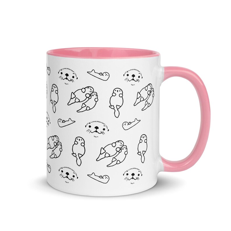 May include: White ceramic mug with a pink interior and handle. The mug features a repeating pattern of black line drawings of otters in various poses. The otters have small, detailed faces and are in different positions.