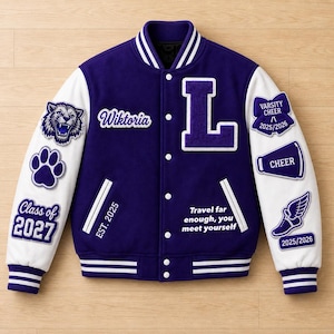 Könnte beinhalten: Eine lila-weiße Collegejacke mit dem Namen "Wiktoria" und dem Buchstaben "L" auf der Vorderseite. Die Jacke hat Aufnäher mit "Class of 2027", "Varsity Cheer" und "2025/2026". Der Text "Travel far enough, you meet yourself" ist ebenfalls vorhanden.
