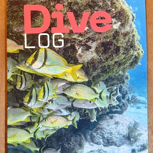 Puede incluir: Un cuaderno de bitácora de buceo con una vibrante escena submarina. La portada presenta un banco de peces amarillos y plateados nadando cerca de un arrecife de coral. Las palabras "Dive LOG" están impresas en letras grandes, rojas y blancas.