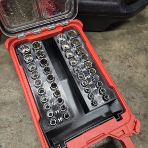 May include: A red plastic carrying case containing a set of silver metal sockets. The case features two black interior trays holding various socket sizes, with metric measurements ranging from 10 to 24 and imperial sizes from 5/16 to 1 inch.