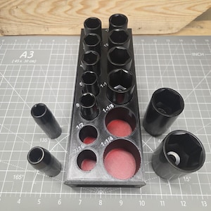 May include: A black socket organizer with various sized sockets. The organizer has labeled slots for sockets ranging from 7/16 to 1-1/4 inches. Several loose sockets are also present, along with a ruler marked in inches.