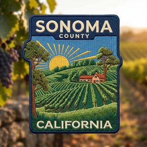 May include: A rectangular embroidered patch featuring a landscape of rolling green vineyards under a yellow sun. The text SONOMA COUNTY is stitched in cream at the top, and CALIFORNIA is stitched in cream at the bottom, with a house.