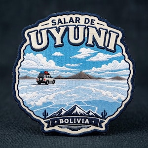 May include: A circular embroidered patch featuring a landscape of the Salar de Uyuni in Bolivia. The design includes a white off-road vehicle on a salt flat, distant mountains, a blue sky with white clouds, and the text Salar de Uyuni and Bolivia.