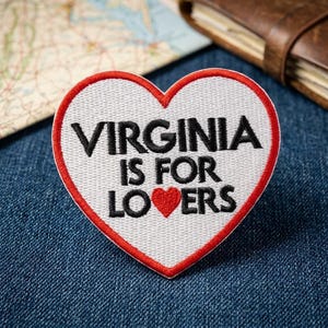 May include: A heart-shaped embroidered patch with a white background and a red border. The text VIRGINIA IS FOR LOVERS is stitched in black, with a small red heart replacing the letter O in the word LOVERS, creating a clear graphic design.
