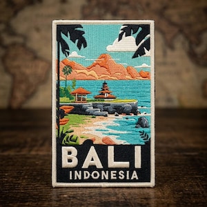 May include: A rectangular embroidered patch featuring a scenic landscape of Bali, Indonesia. The design depicts a temple by the sea, orange mountains, palm trees, and blue water. The word BALI is in large white letters above INDONESIA in smaller text.