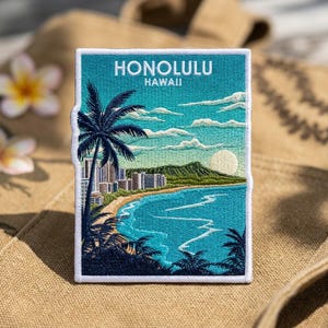 May include: A rectangular embroidered patch featuring a scenic view of Honolulu, Hawaii. The design displays a turquoise ocean, a sandy beach, a green mountain, and a palm tree in the foreground. The text HONOLULU HAWAII is stitched in white.
