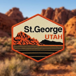 May include: A hexagonal embroidered patch featuring a cream-colored background with the black text St. George and orange text UTAH. The design includes a stylized orange mountain range, a black silhouette of hills, and horizontal black and orange lines.