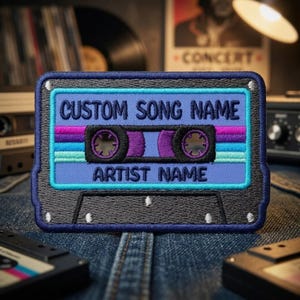 May include: A rectangular embroidered patch shaped like a cassette tape with a dark blue border. The center features a light blue background with horizontal stripes in purple and teal, displaying the text CUSTOM SONG NAME and ARTIST NAME.
