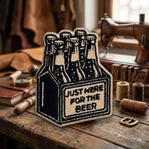 May include: An embroidered patch featuring a six-pack of beer bottles in black and tan thread. The design includes the text 'JUST HERE FOR THE BEER' printed in bold, black capital letters on the front of the carrier, with a tan border.