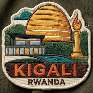 May include: An embroidered patch featuring a large golden beehive structure, a modern building, and a torch with a flame. The design includes green hills, a blue stream, and the text KIGALI RWANDA in orange and brown thread on a cream background.