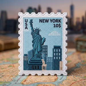 May include: A rectangular embroidered patch shaped like a postage stamp featuring the Statue of Liberty in teal thread against a light blue background. The text USA, NEW YORK, and 10$ are stitched in black. It has a white scalloped border.