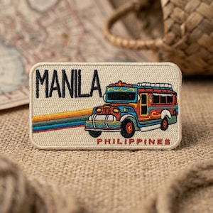 May include: A rectangular embroidered patch featuring a colorful jeepney illustration with a rainbow stripe. The text MANILA is embroidered in large black letters on the left, and the word PHILIPPINES is in smaller red letters at the bottom.