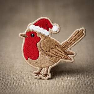 May include: An embroidered patch of a robin bird featuring a bright red chest, light brown wings, and a small red Santa hat with a white trim and pom-pom. The bird has a black eye and a pointed beak, with detailed stitching throughout the design.
