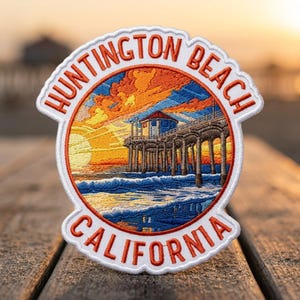 May include: A circular embroidered patch featuring a sunset scene over the Huntington Beach pier in California. The text HUNTINGTON BEACH and CALIFORNIA is stitched in orange thread along the top and bottom borders of the white-edged patch.