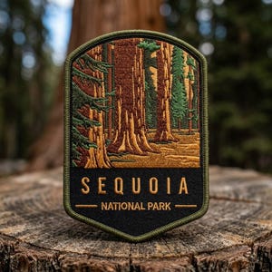 May include: A shield-shaped embroidered patch featuring a forest of tall brown sequoia trees and green pine branches. The bottom section is black with the gold text "SEQUOIA" above the words "NATIONAL PARK" separated by a horizontal line.
