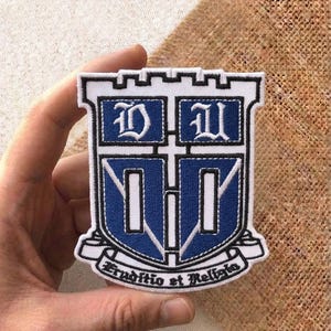 May include: Embroidered patch featuring a shield design with the letters "D" and "U" in white on a blue background. The patch has a white border and the Latin phrase "Eruditio et Religio" is written on a banner at the bottom.