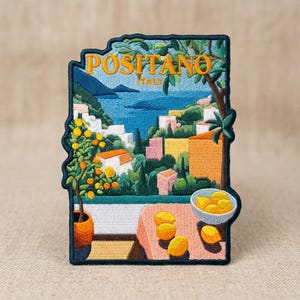 May include: A rectangular embroidered patch featuring a scenic view of Positano, Italy. The design includes a coastal landscape with colorful buildings, a blue sea, a lemon tree in a pot, and a table with a bowl of lemons and loose lemons.