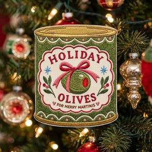 May include: A rectangular embroidered patch shaped like a can, featuring a green background with gold trim. The center displays a cream-colored label with the text HOLIDAY OLIVES FOR MERRY MARTINIS, a red bow, a green olive, and small sprigs.