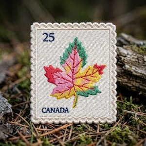 May include: A rectangular embroidered patch with a scalloped edge, featuring a cream-colored background. It displays a multi-colored maple leaf in shades of red, pink, yellow, and green. The text 25 and CANADA are stitched in dark blue.