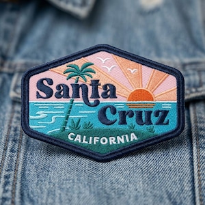 May include: A hexagonal embroidered patch featuring a sunset scene with a palm tree, ocean waves, and three birds. The text reads Santa Cruz in dark blue script and CALIFORNIA in white block letters. The patch has a dark blue border.