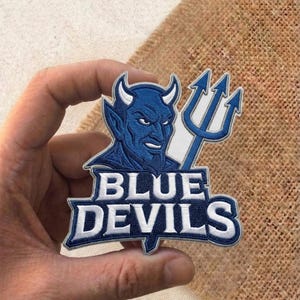 May include: A white ceramic mug with a black handle and the text "But First, Coffee" in a black, handwritten-style font. The mug is on a white surface.