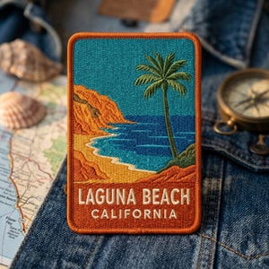 May include: A rectangular embroidered patch featuring a coastal scene with a palm tree, blue ocean, and orange cliffs. The text LAGUNA BEACH CALIFORNIA is stitched in white at the bottom against a dark orange background with a thick orange border.