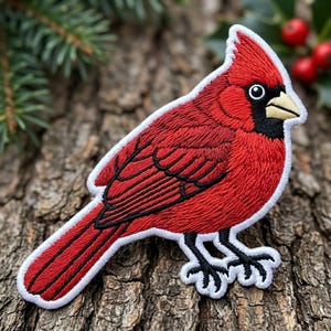May include: An embroidered patch shaped like a northern cardinal bird. The bird features vibrant red plumage, a black mask around its eyes, a pointed crest on its head, and a light tan beak. The patch is outlined with a thick white border.