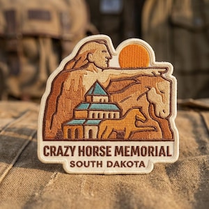 May include: Embroidered patch featuring the Crazy Horse Memorial in South Dakota. The design includes a profile of Crazy Horse, a building, a horse, and a setting sun. The text "Crazy Horse Memorial" and "South Dakota" are displayed below the image.