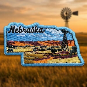 May include: An embroidered patch shaped like the state of Nebraska with a light blue border. The design features a landscape with yellow fields, dark purple shadows, and a black windmill silhouette under a blue sky with the word Nebraska.